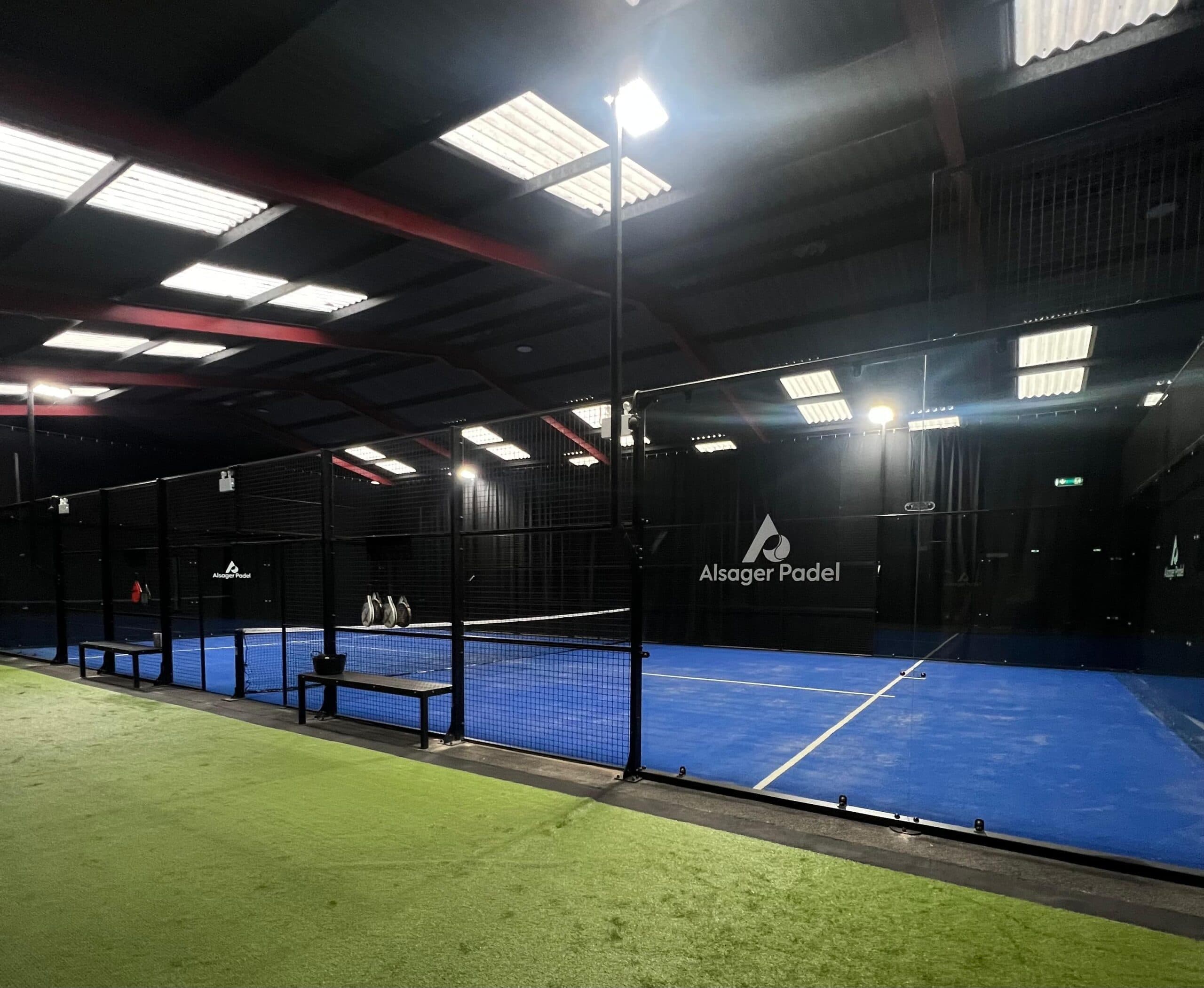 An indoor padel court with blue playing surfaces and glass walls